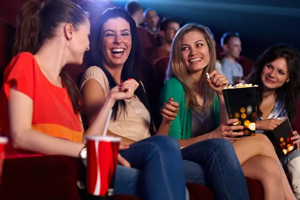 Happy girls sitting in multiplex movie theater, talking, laughing