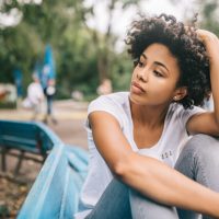 Attractive Afro American woman sitting on bench outdoors in the park feeling dissapointed aftre conversation with friend