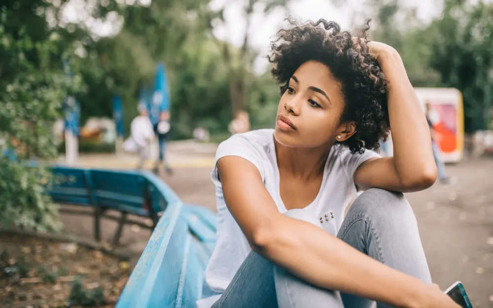 Attractive Afro American woman sitting on bench outdoors in the park feeling dissapointed aftre conversation with friend