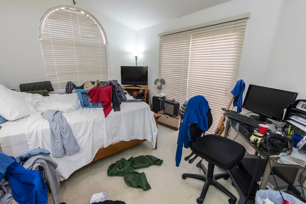 Cluttered, messy bedroom with piles of clothes, music and sports equipment.