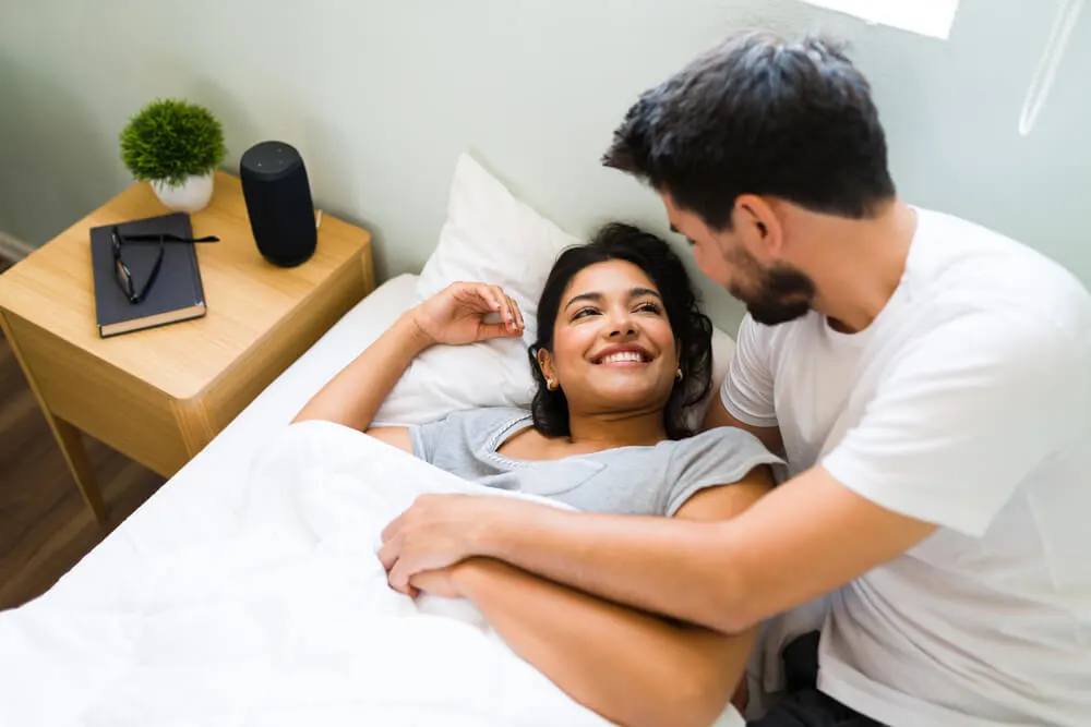 Hispanic boyfriend smiling to his girlfriend after waking her up