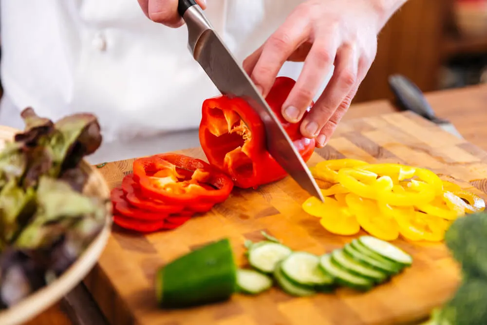 Closeup of hands of chef cook cutting vegetables on wooden table