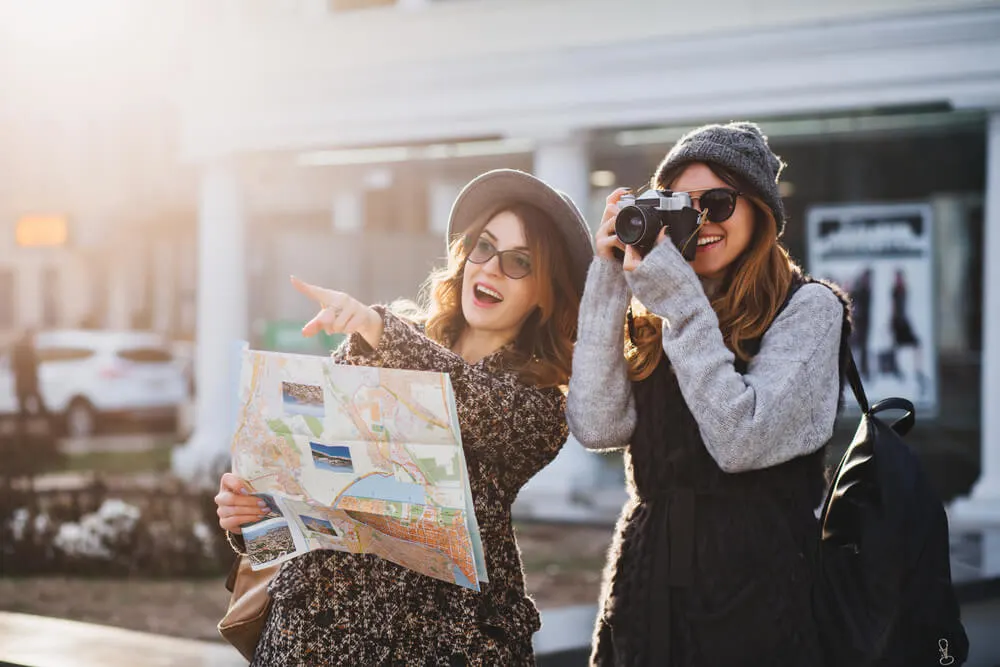 Happy travel together of two fashionable girls in sunny city centre.