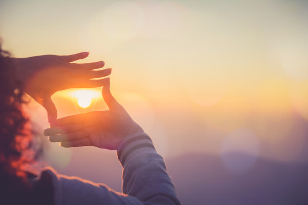 The woman making frame round the sun with her hands in sunrise