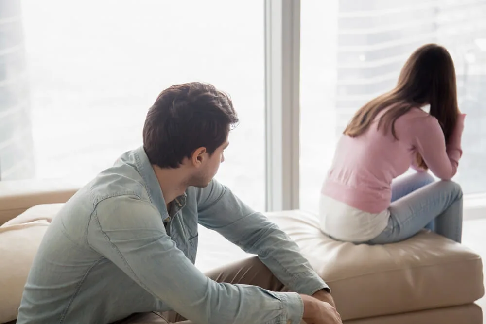 Young couple sitting apart indoors after quarrel