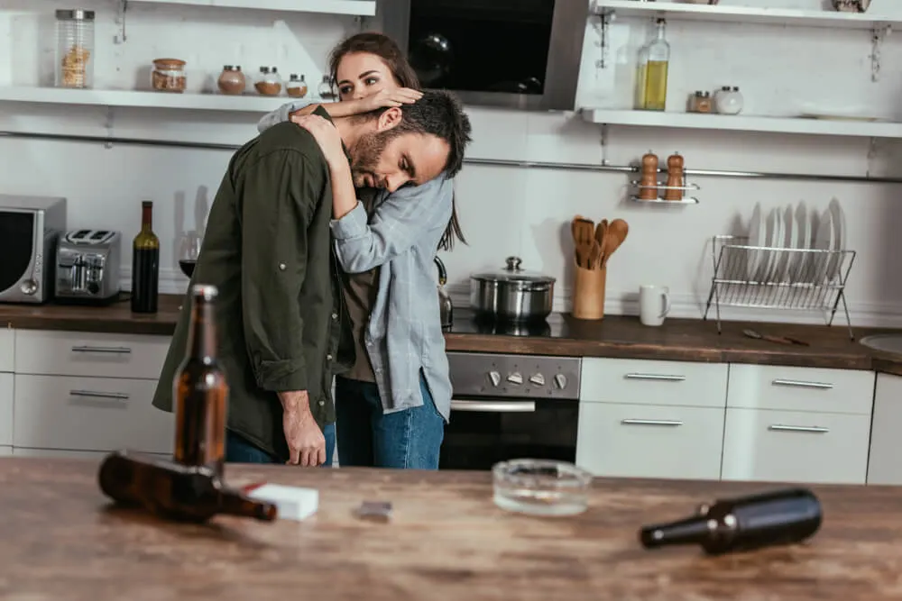 Selective focus of woman calming down worried husband with alcohol addiction