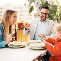 Young couple with kid eating pasta in the restaurant