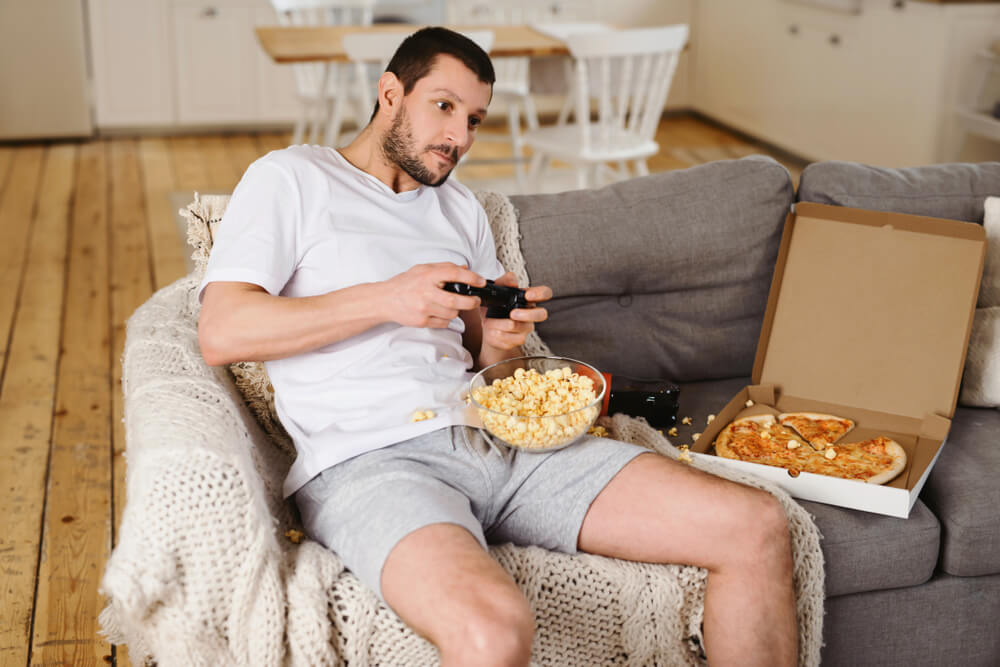 Man playing a video games eating popcorn and pizza
