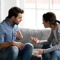 Stressed young married family couple arguing emotionally, blaming lecturing each other, sitting on couch