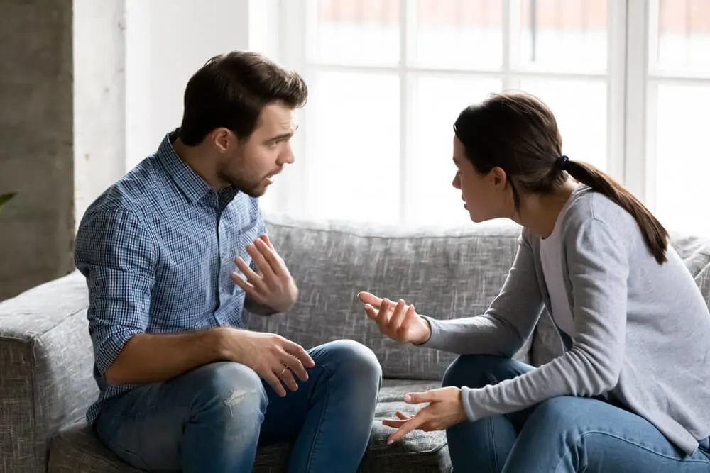 Stressed young married family couple arguing emotionally, blaming lecturing each other, sitting on couch.