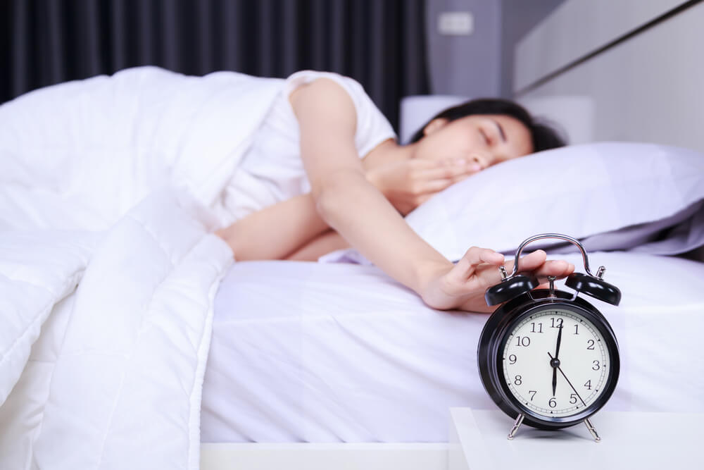 Woman yawing on bed and rise hand to turn off alarm clock in the bedroom