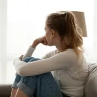 Side view young woman looking away at window sitting on couch at home