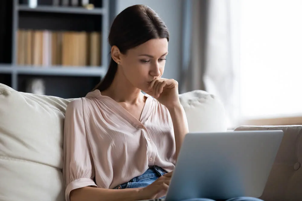 Close up thoughtful upset woman looking at laptop screen, pondering ideas or difficult tasks