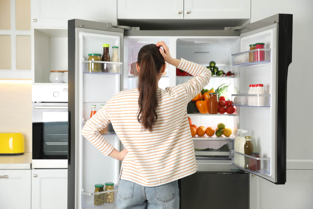 Young woman near open refrigerator in kitchen