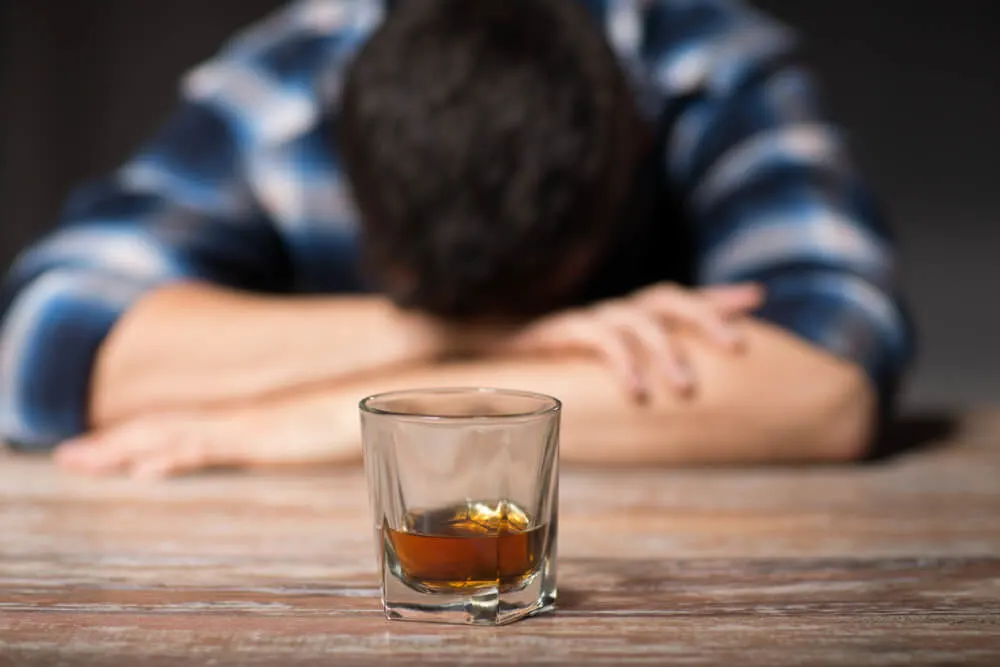 male alcoholic with glass of whiskey lying or sleeping on table at night