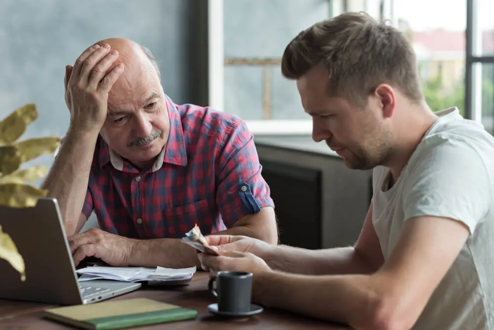 Sad and stressed elderly father and his adult son counting money