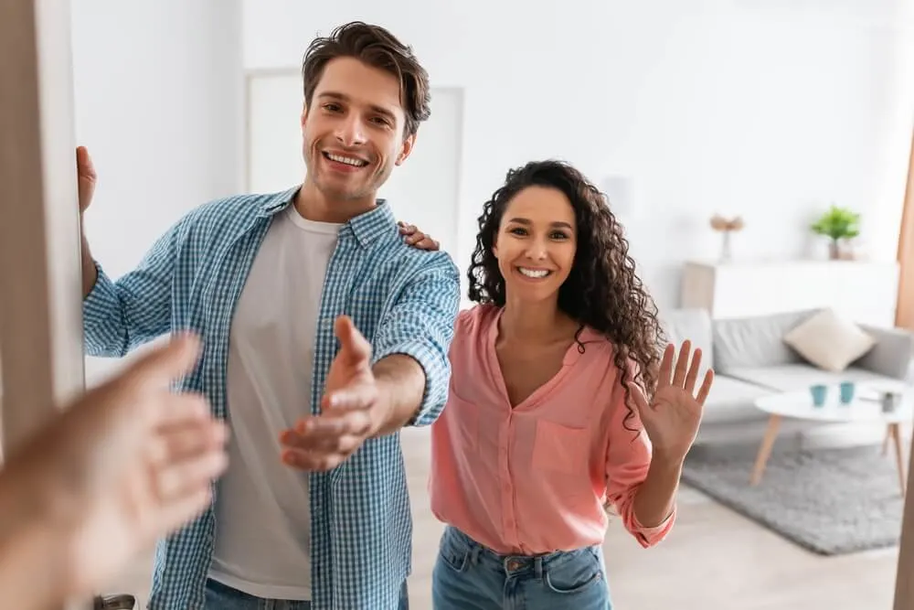 Portrait of cheerful couple inviting guests to enter home