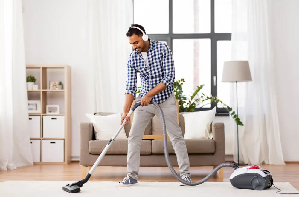 indian man in headphones with vacuum cleaner at home