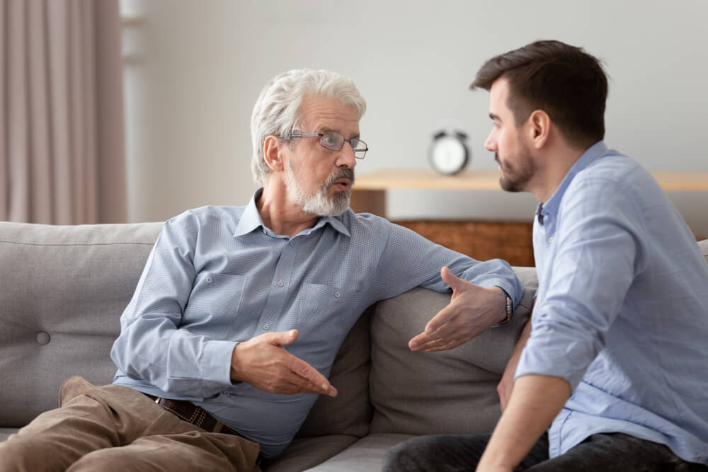 elderly father and grown up adult son sitting on sofa