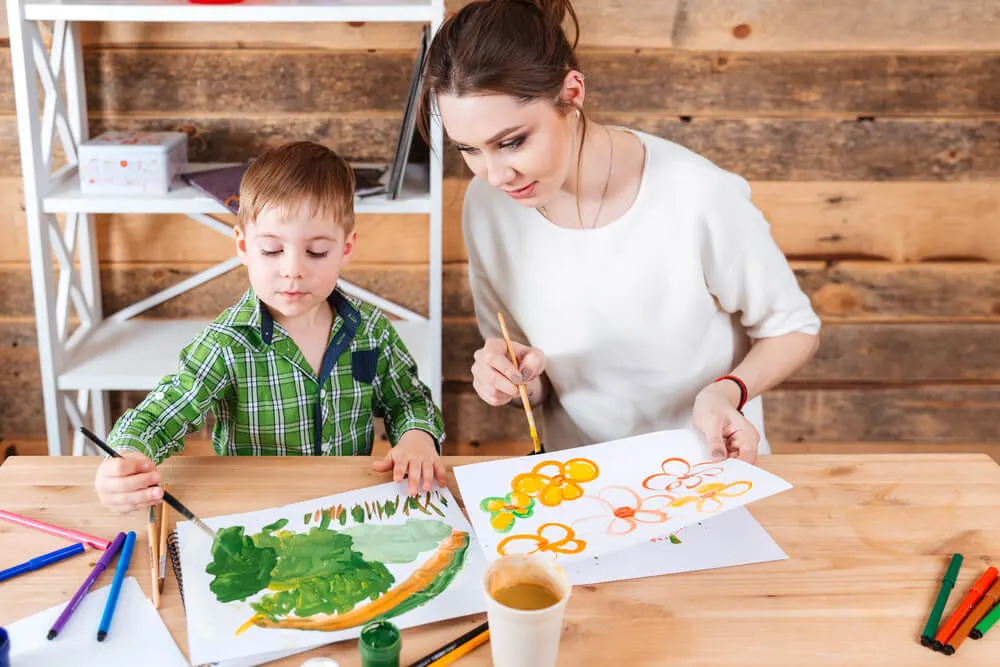Cute little boy and his mother sitting and paiting bright pictures together