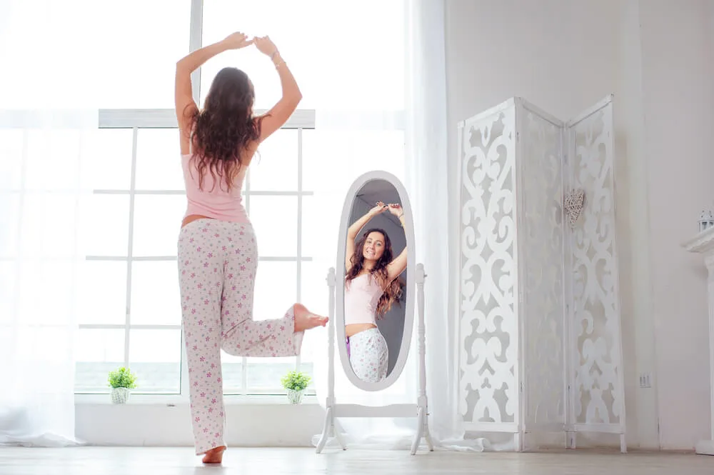 Attractive young woman dancing near mirror at her apartment