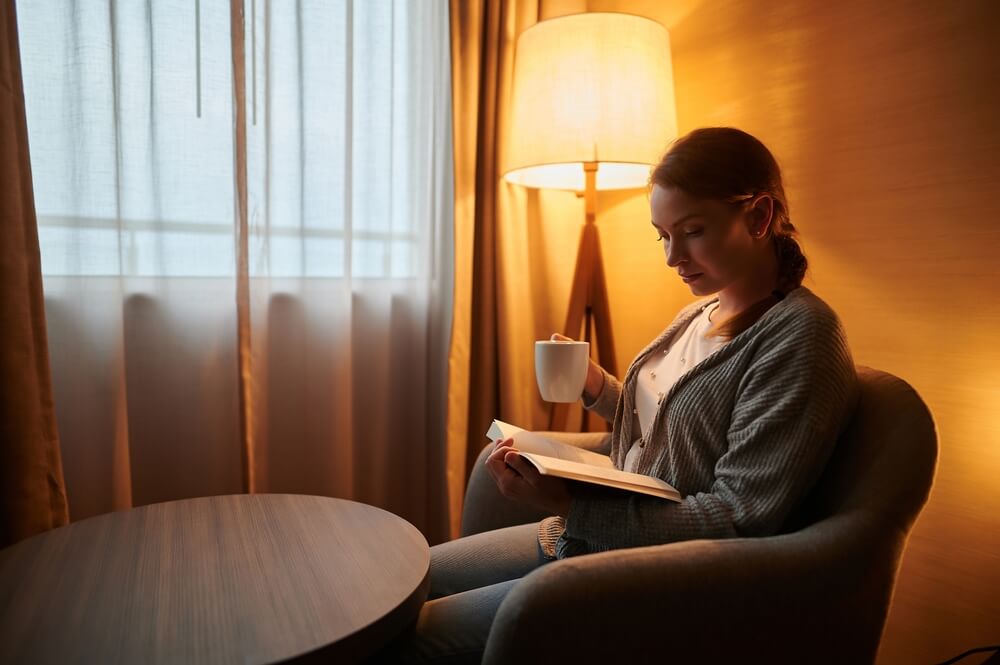 A young woman is sitting in a room with a cup of coffee and reading a book