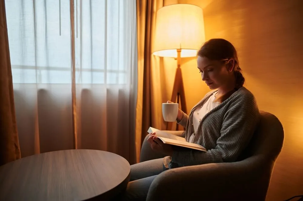 A young woman is sitting in a room with a cup of coffee and reading a book
