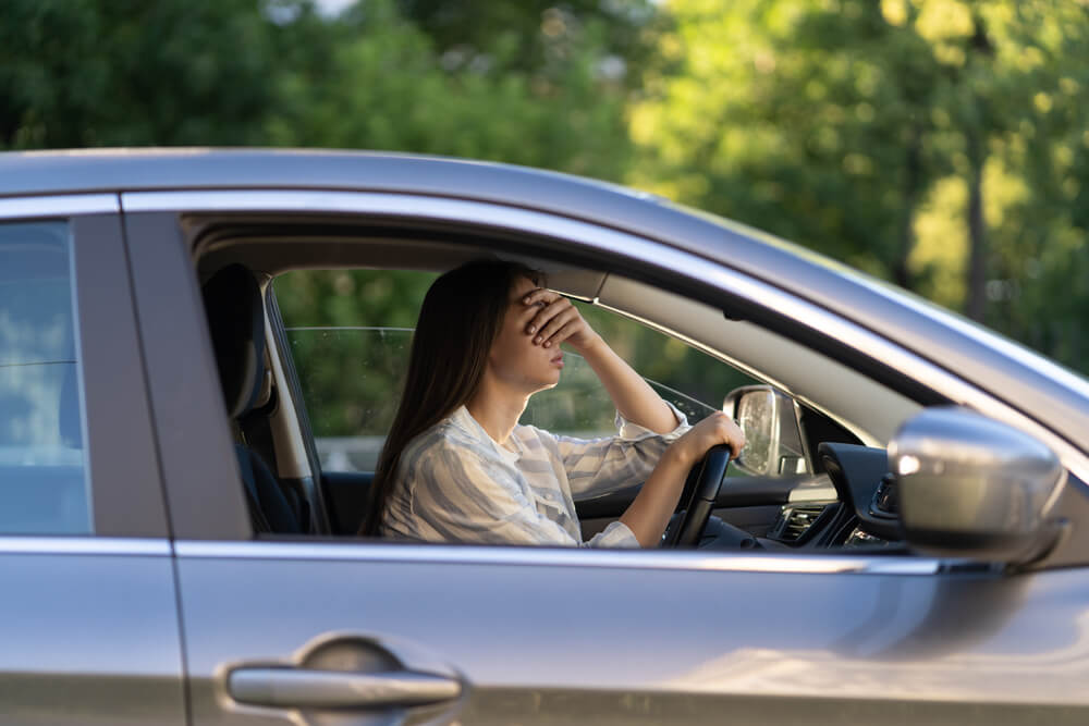 Stressed girl with headache driving car touching forehead with hand