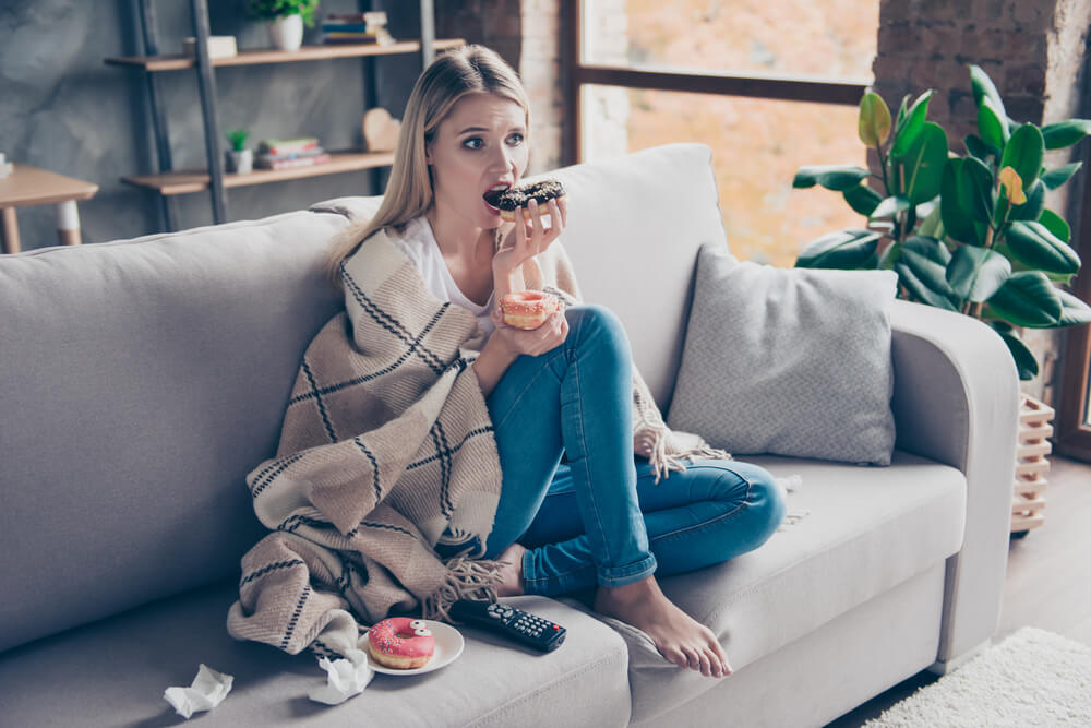 Woman sitting on couch in living room and eating donat 