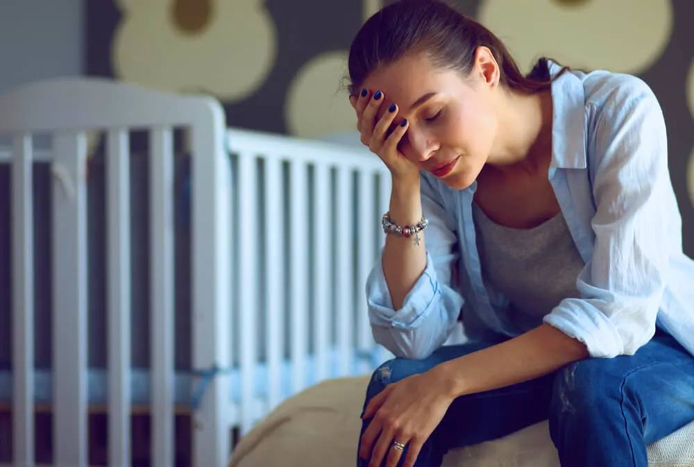 My Wife Doesn't Want to Spend Time With Me - What Can I Do? 1 Young tired woman sitting on the bed near children's cot.