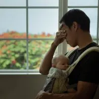 A tired stressed out father holding his sleeping baby at home