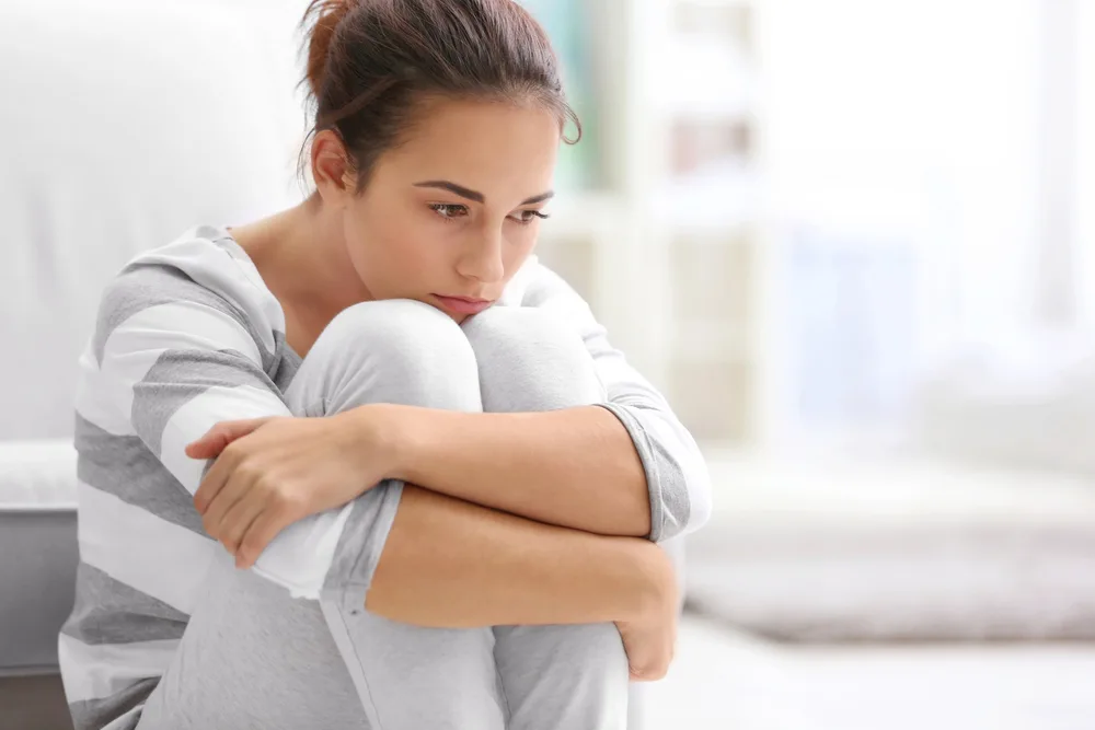 Depressed young woman sitting on floor at home