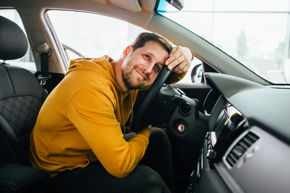 Young worried funny looking man obsessing about cleanliness of his new car on a summer day.