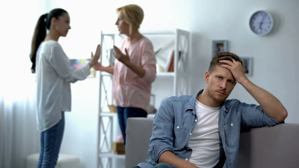 Exhausted male listening wife and mother-in-law arguing at home