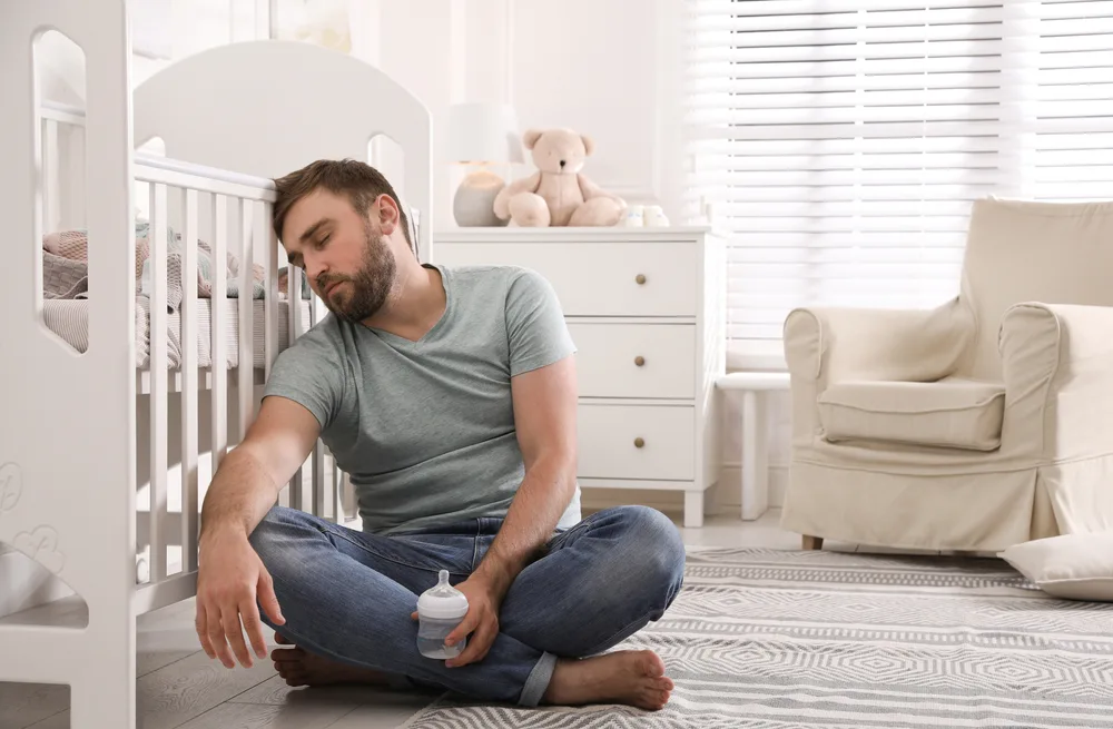 Tired father with bottle of milk sleeping on floor