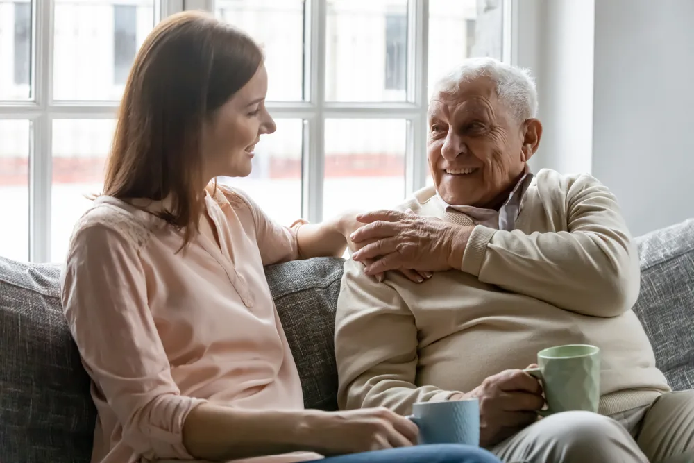 Smiling young woman sitting on sofa with happy older father