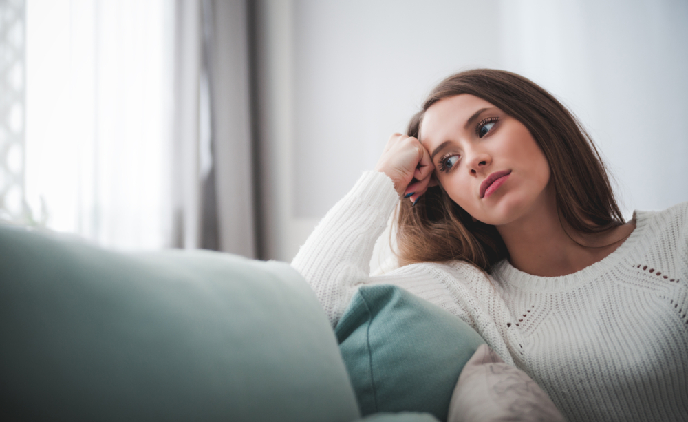 Sad woman sitting on sofa at home deep in thoughts