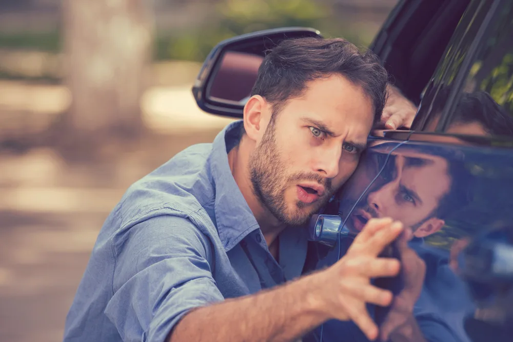 Young worried funny looking man obsessing about the cleanliness of his new car