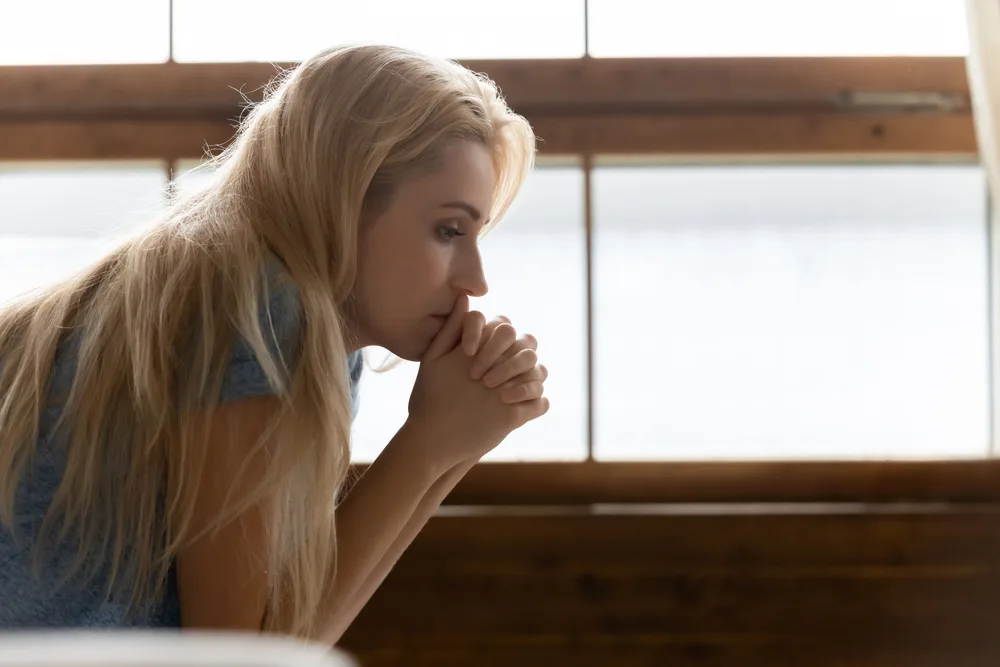 Side shot of thoughtful pensive sad young female sitting indoors feeling unhappy