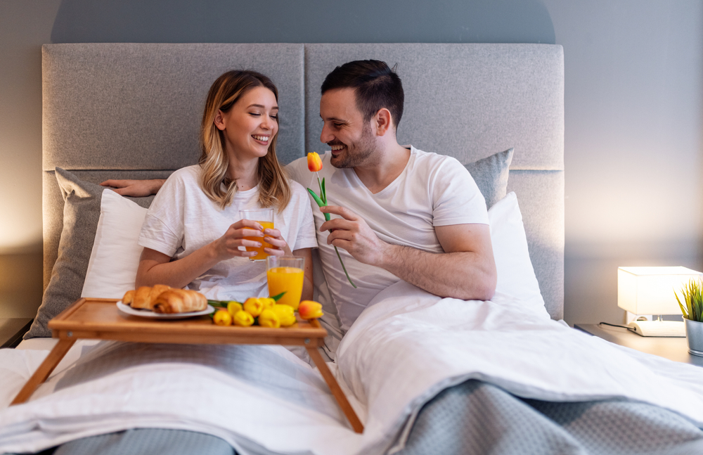 Beautiful smiling young couple having breakfast in bedroom